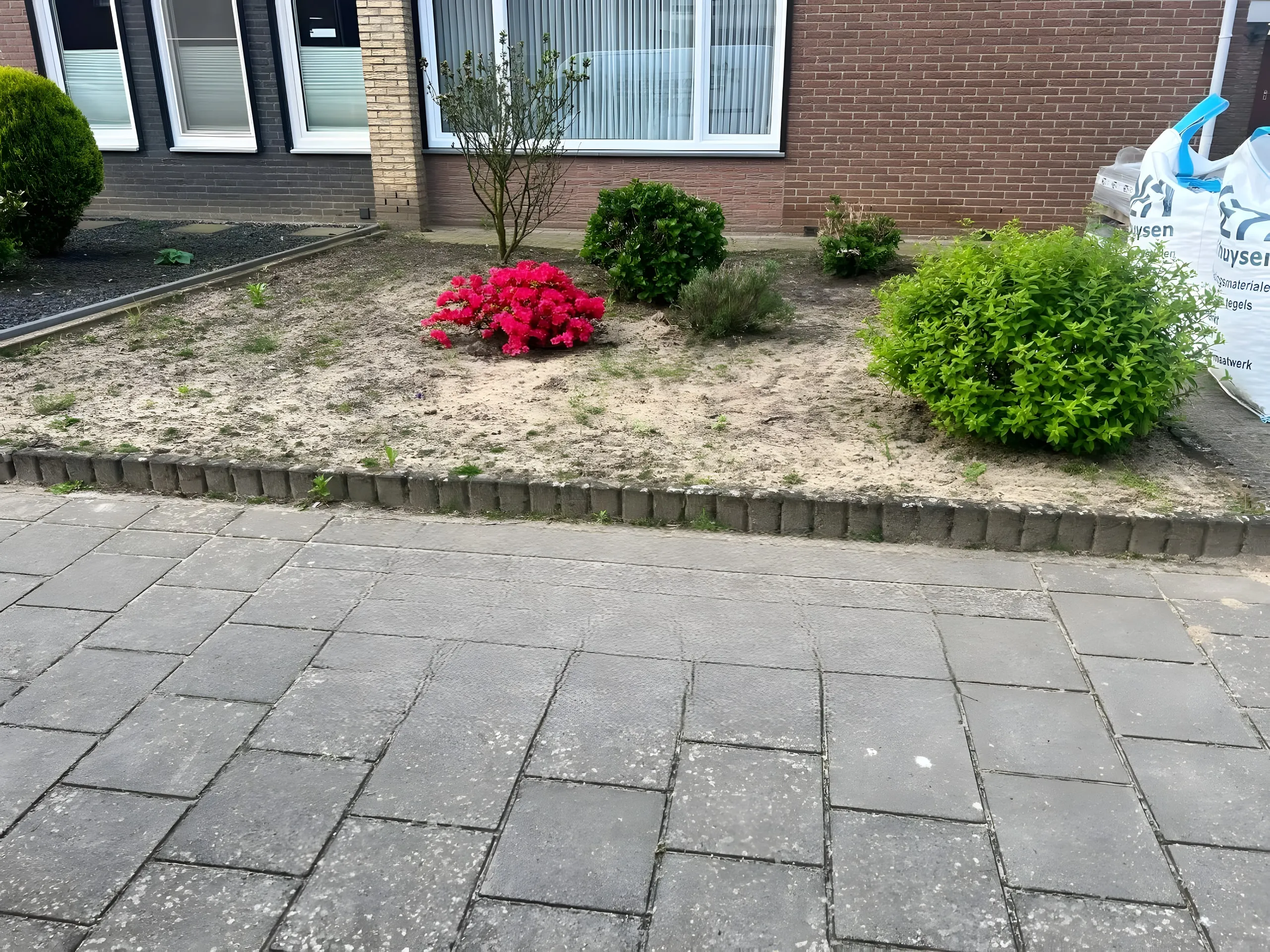 De voortuin voor de aanleg: kaal plantvak en verweerde tegels
